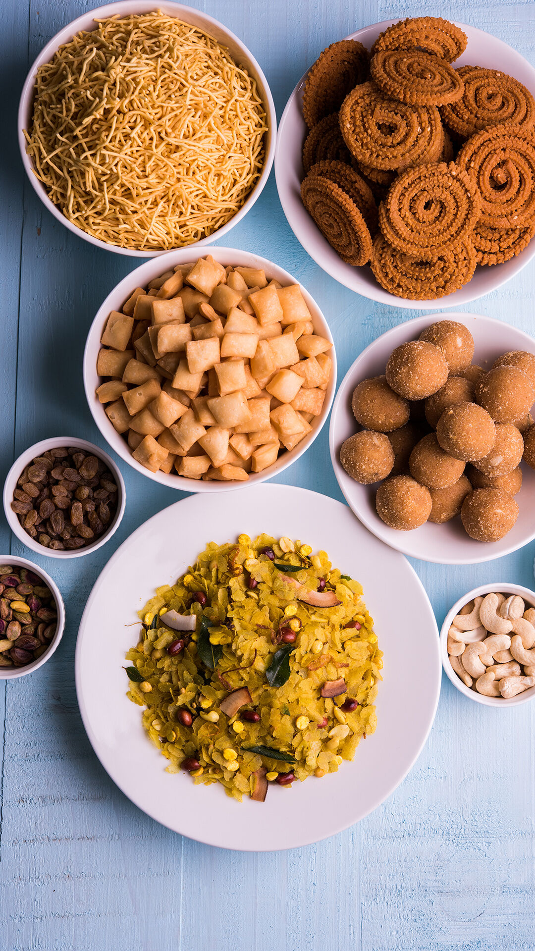 Traditional Diwali snacks platter with poha chivda, chakli, shankarpali, ladoo, sev, dry fruits, and nuts on festive blue background